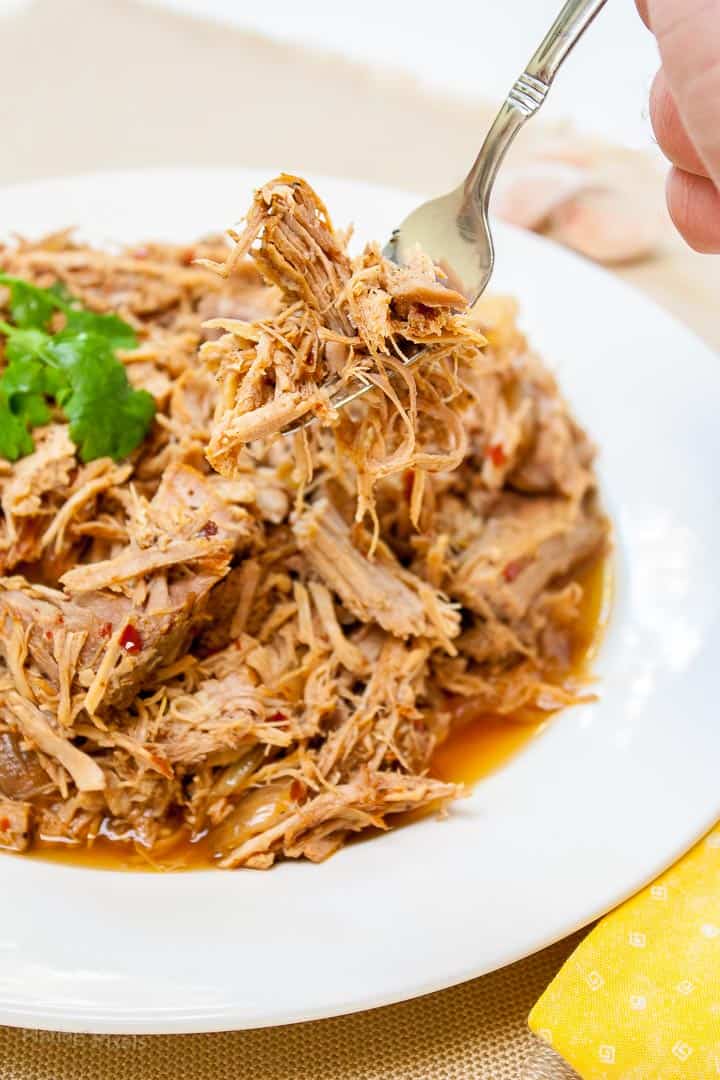 Carolina Style Slow Cooker Pulled Pork on a plate with a hand using fork to pick some up