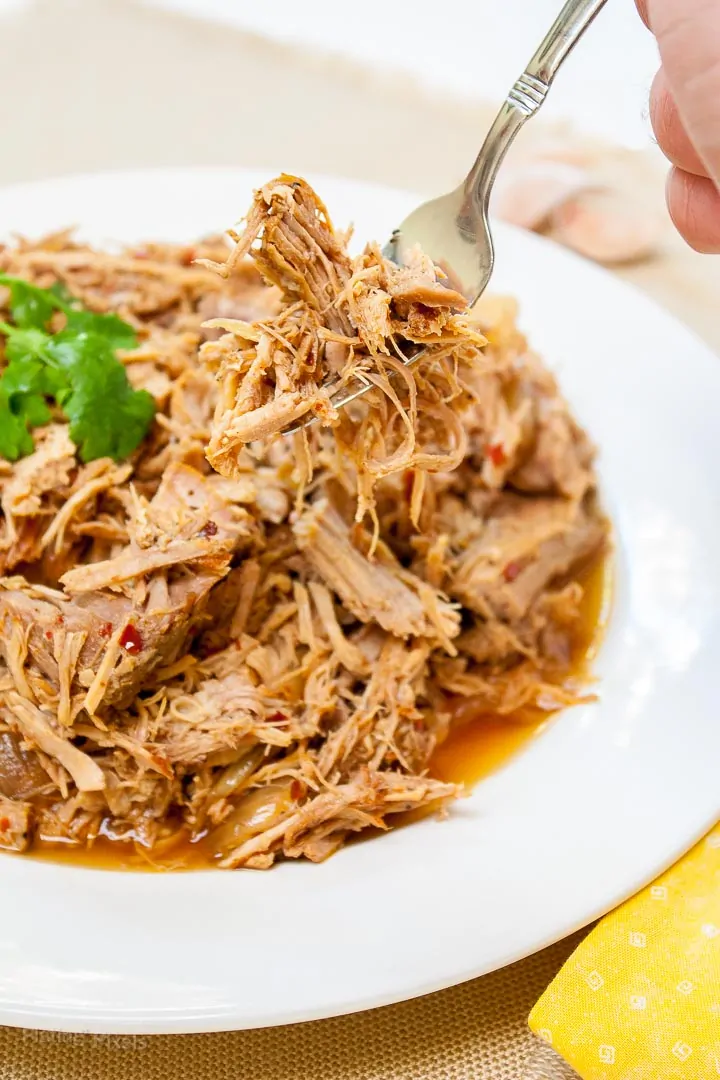 Carolina Style Slow Cooker Pulled Pork on a plate with a hand using fork to pick some up