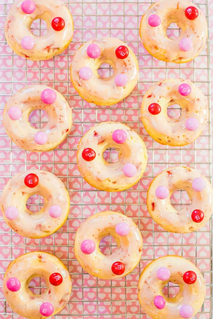 An overhead shot of Strawberry Glazed Baked Doughnuts on a cooling rack topped with pink M&M's