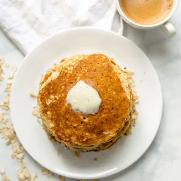 Healthy Banana Oatmeal Pancake on a plate topped with slice of butter next to cup of coffee