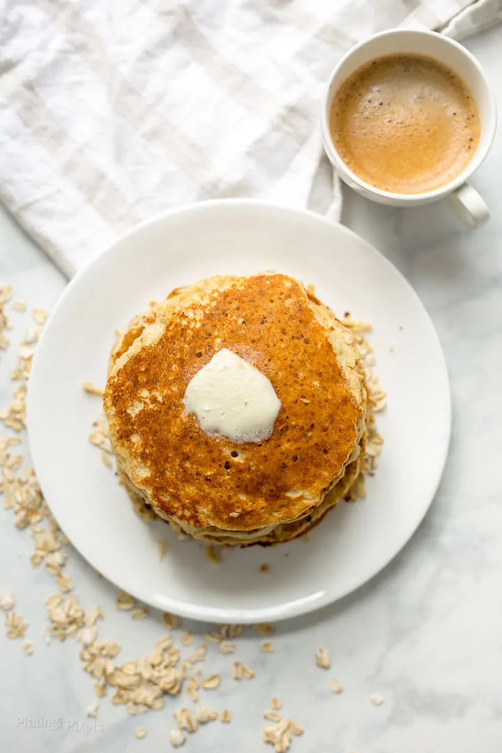 Healthy Banana Oatmeal Pancake on a plate topped with slice of butter next to cup of coffee