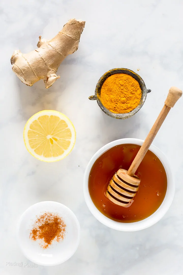 Ingredients to make Immune Boosting Turmeric Tea on a marble table (fresh ginger root, turmeric powder, honey, and cayenne pepper)