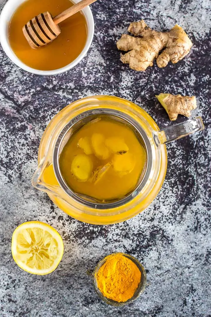 Overhead shot of turmeric tea in a teapot surrounded by ingredients to make it