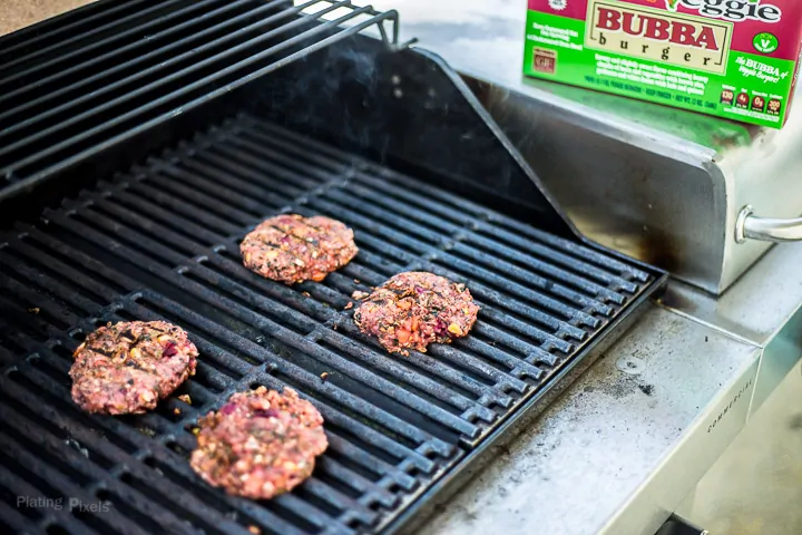 Four veggie burgers cooking on a gas grill