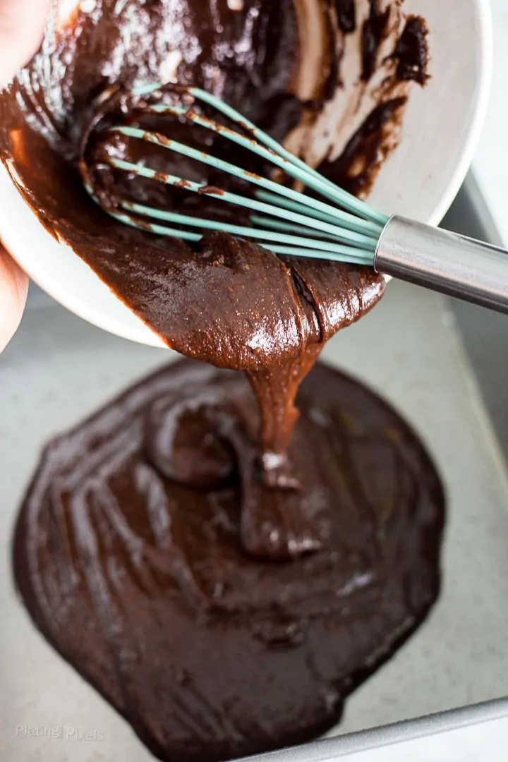 Process shot of pouring brownie batter in a prepared baking pan
