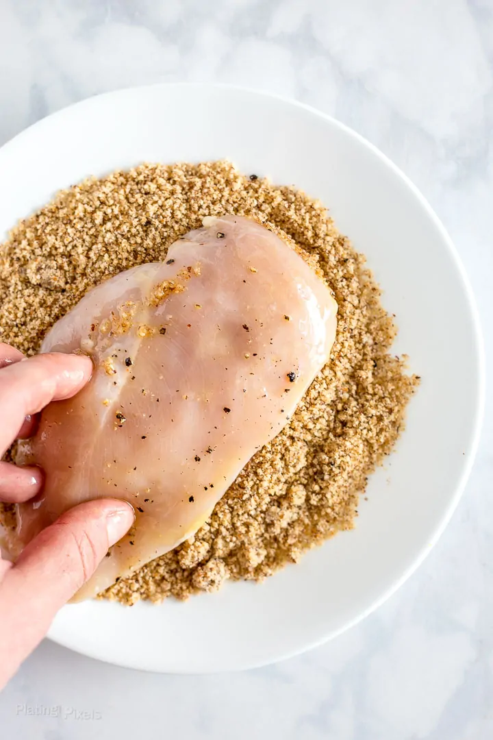 Process shot of coating one side of a chicken breast in keto bread crumbs