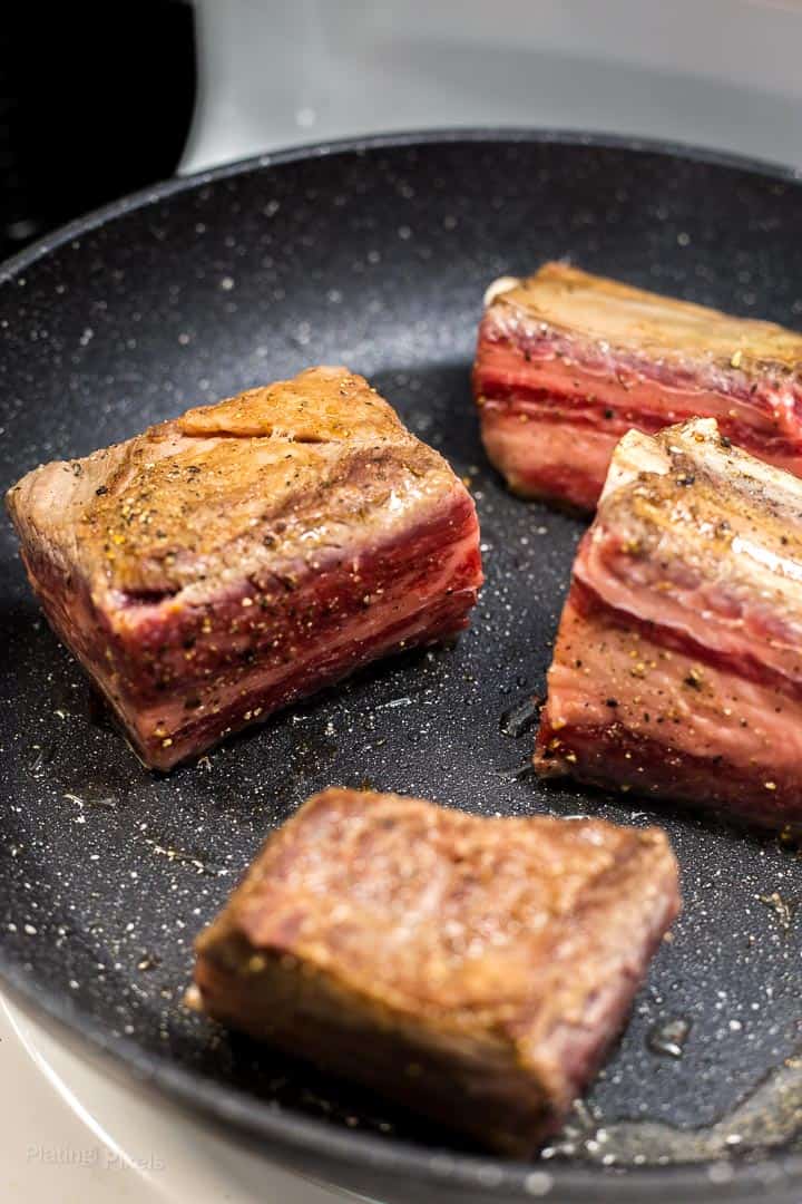 Process shot of browning beef short ribs in a pan before slow cooking