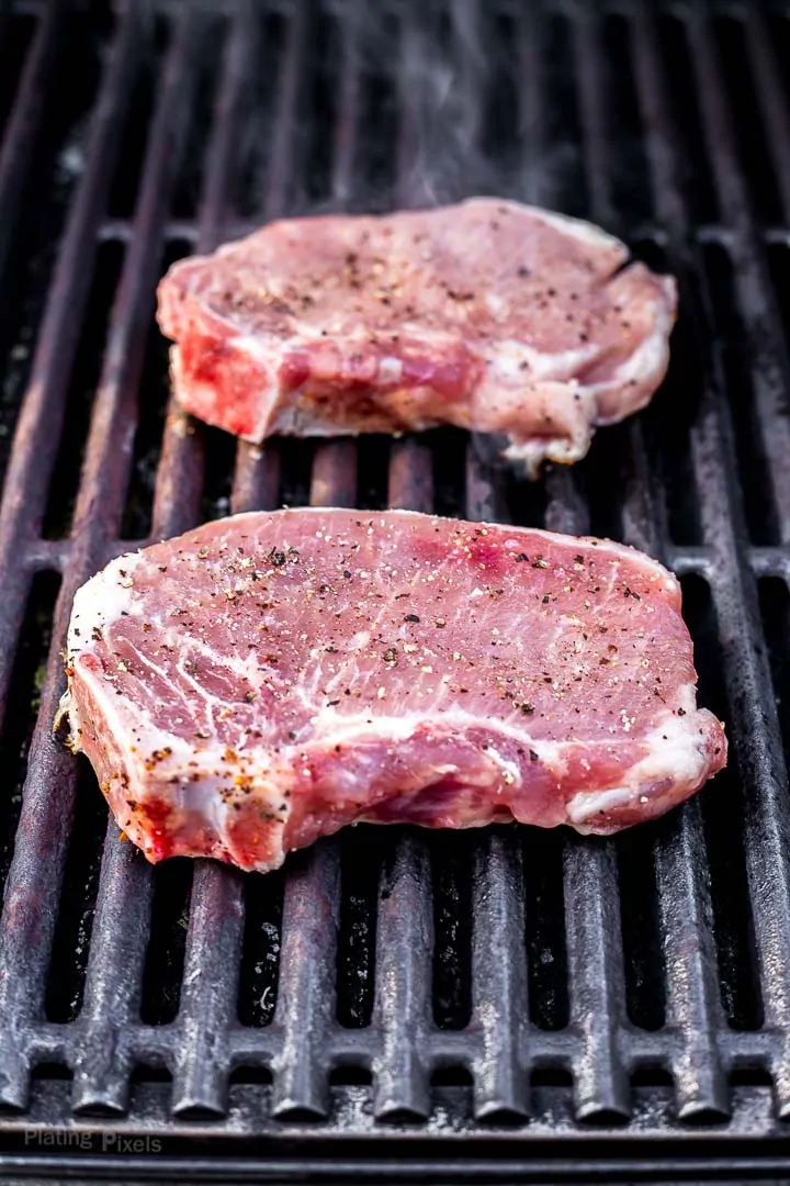 Two pork chop just out on grill with smoke coming off of them