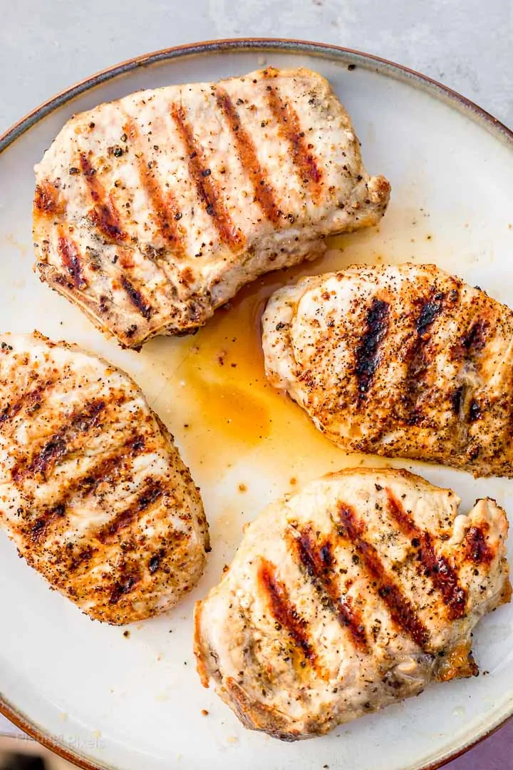 Juicy grilled pork chops resting with some internal juices on the plate