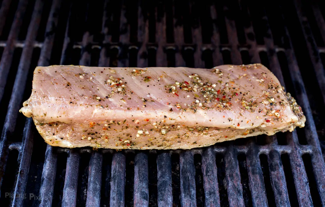 Marinated pork tenderloin just placed on a gas grill