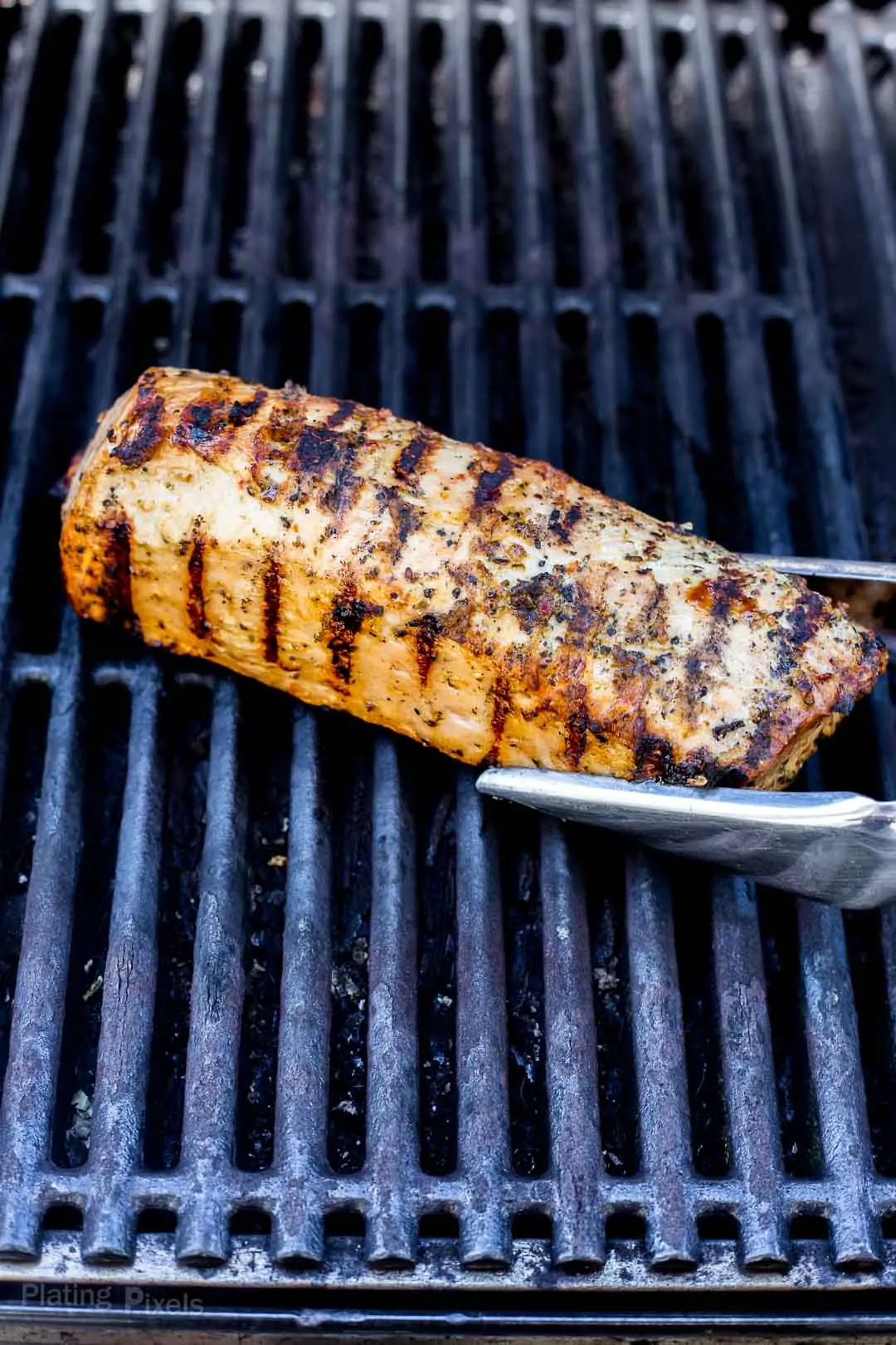 Process shot of rotating a pork tenderloin with nice sear marks on gas grill