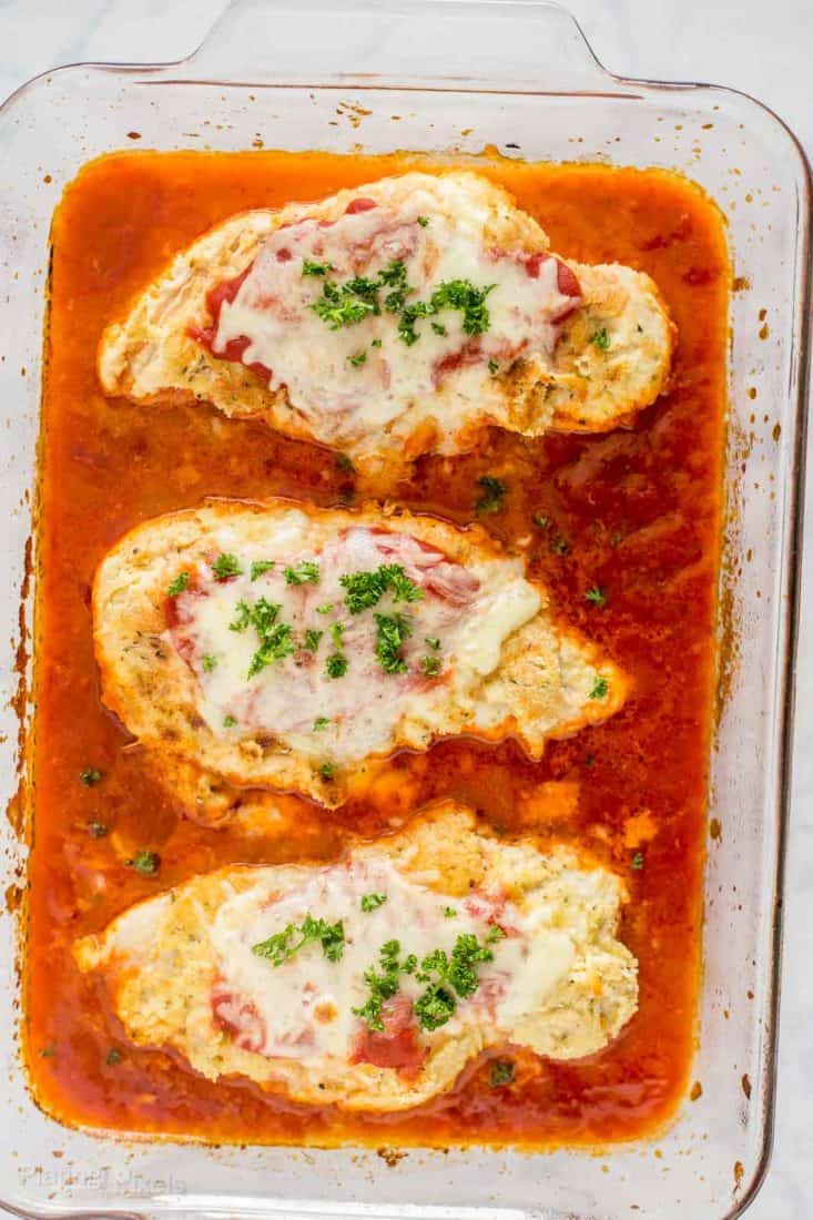 Three Keto Baked Chicken Parmesan breasts in a baking dish over a bed of marinara sauce