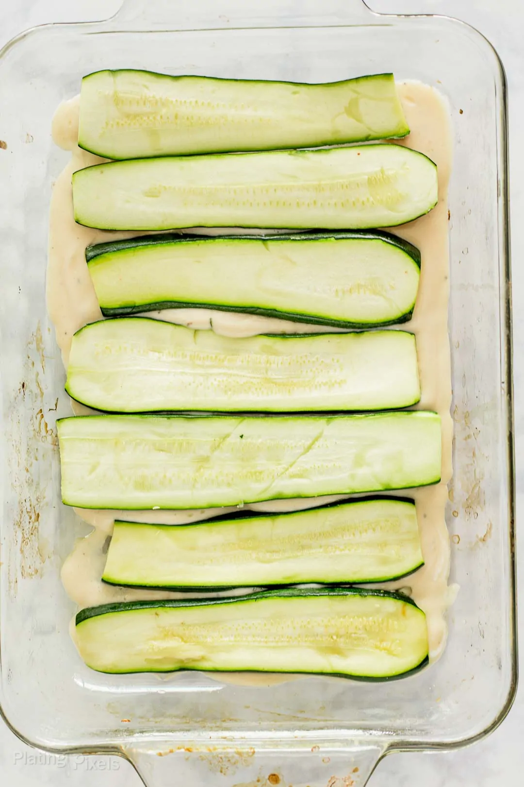 Process shot - zucchini slices and alfredo sauce in a baking dish to make a zucchini lasagna