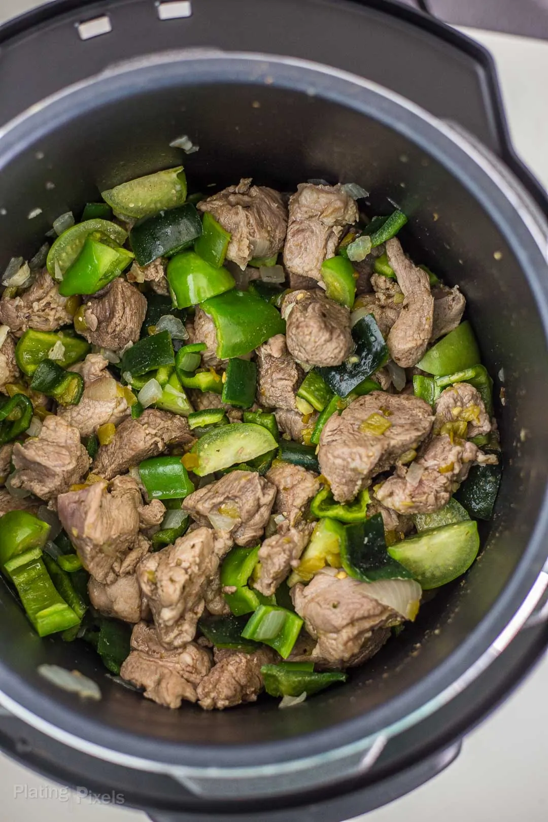 Pork shoulder, chunks tomatillo and peppers in a pressure cooker ready to be cooked