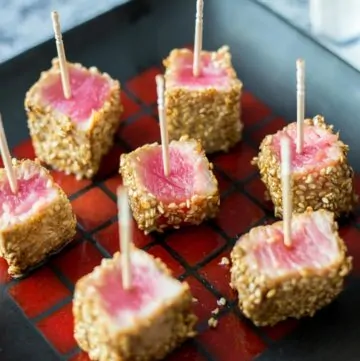Seared Sesame Seared Ahi Tuna Bites on a black plate with toothpicks inserted in them
