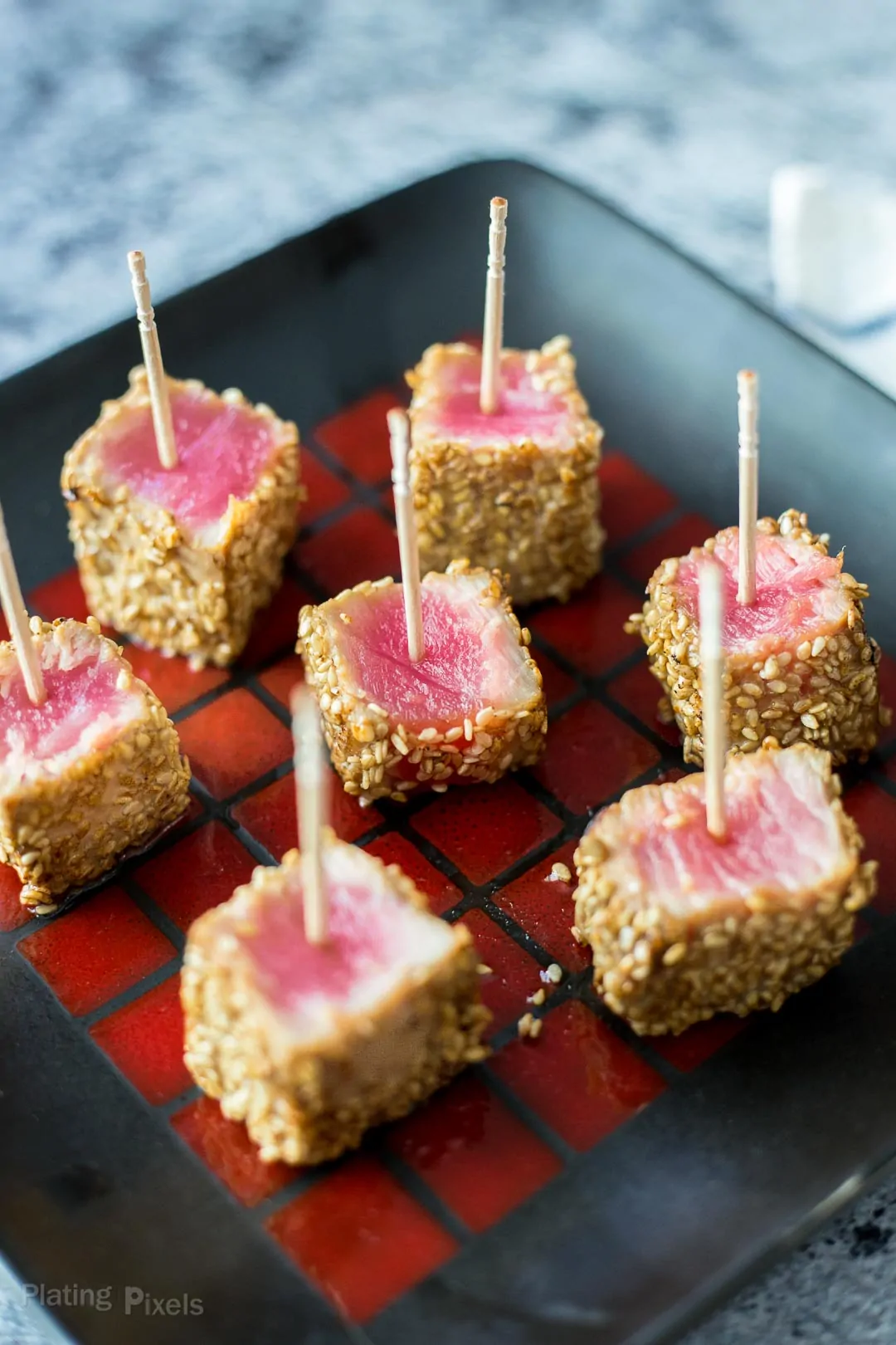 Seared Sesame Seared Ahi Tuna Bites on a black plate with toothpicks inserted in them