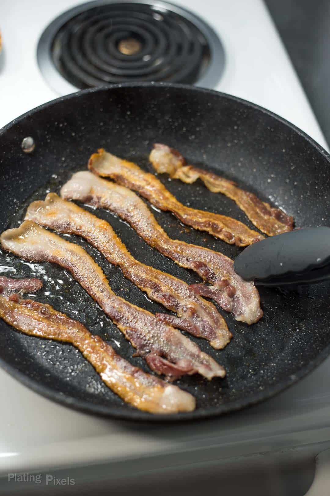 Process shot of cooking bacon in a pan over the stove