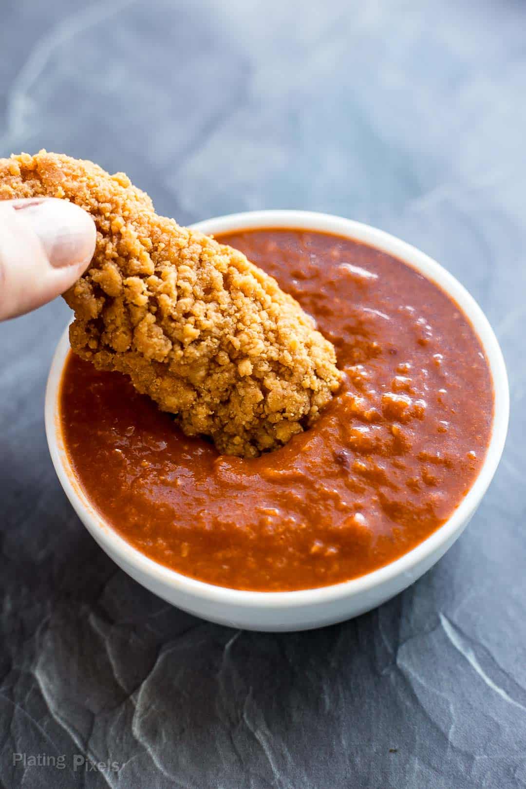 Dipping a crispy chicken strip into homemade barbecue sauce