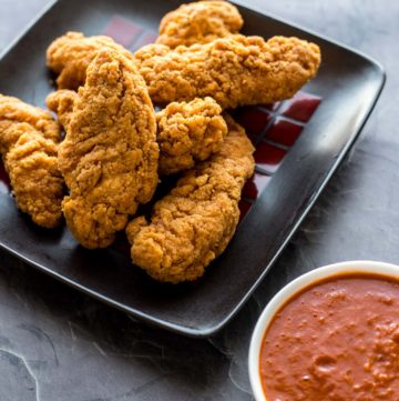 A plate of chicken strips next to homemade barbecue sauce for dipping
