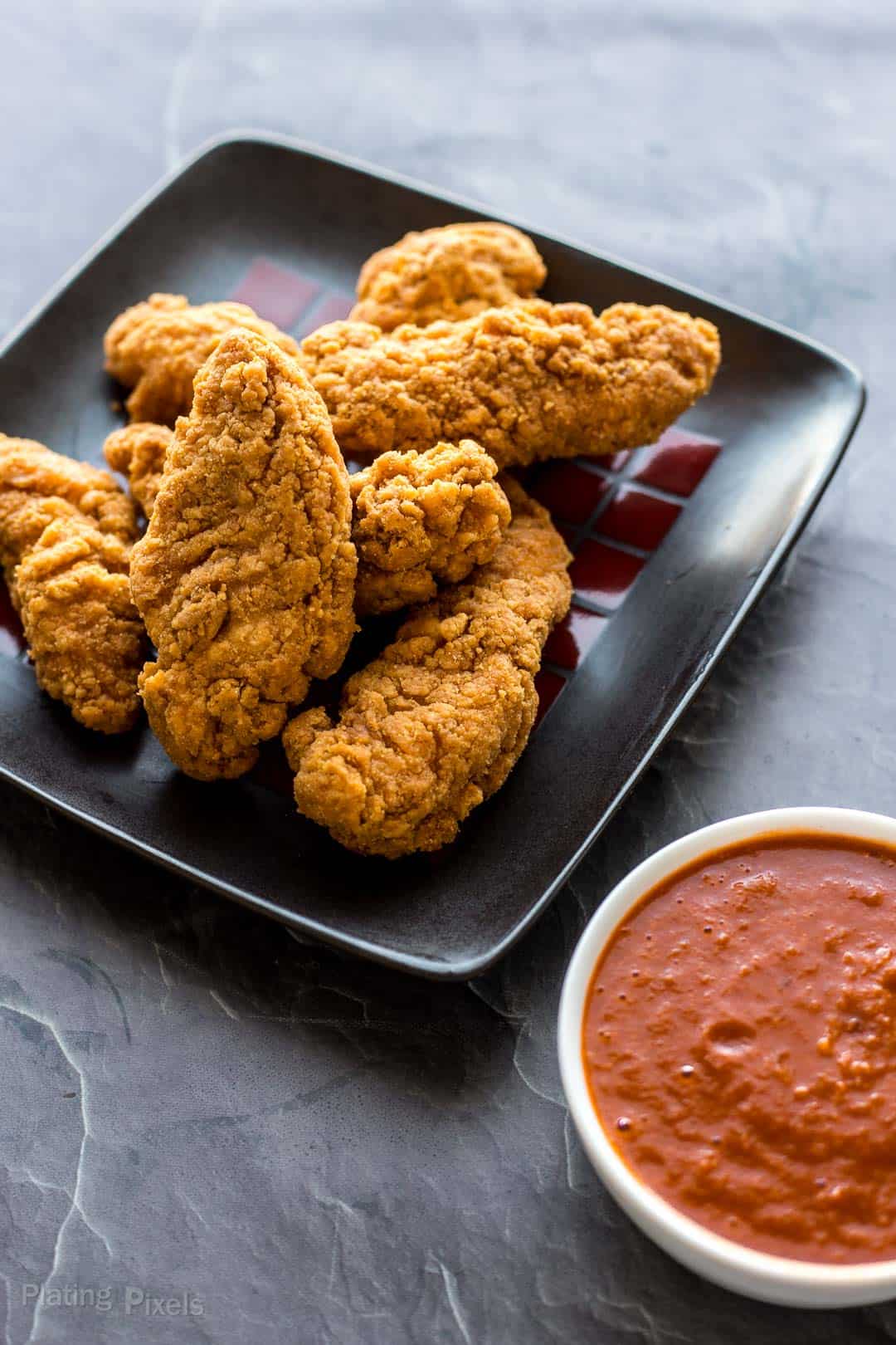 A plate of chicken strips next to homemade barbecue sauce for dipping