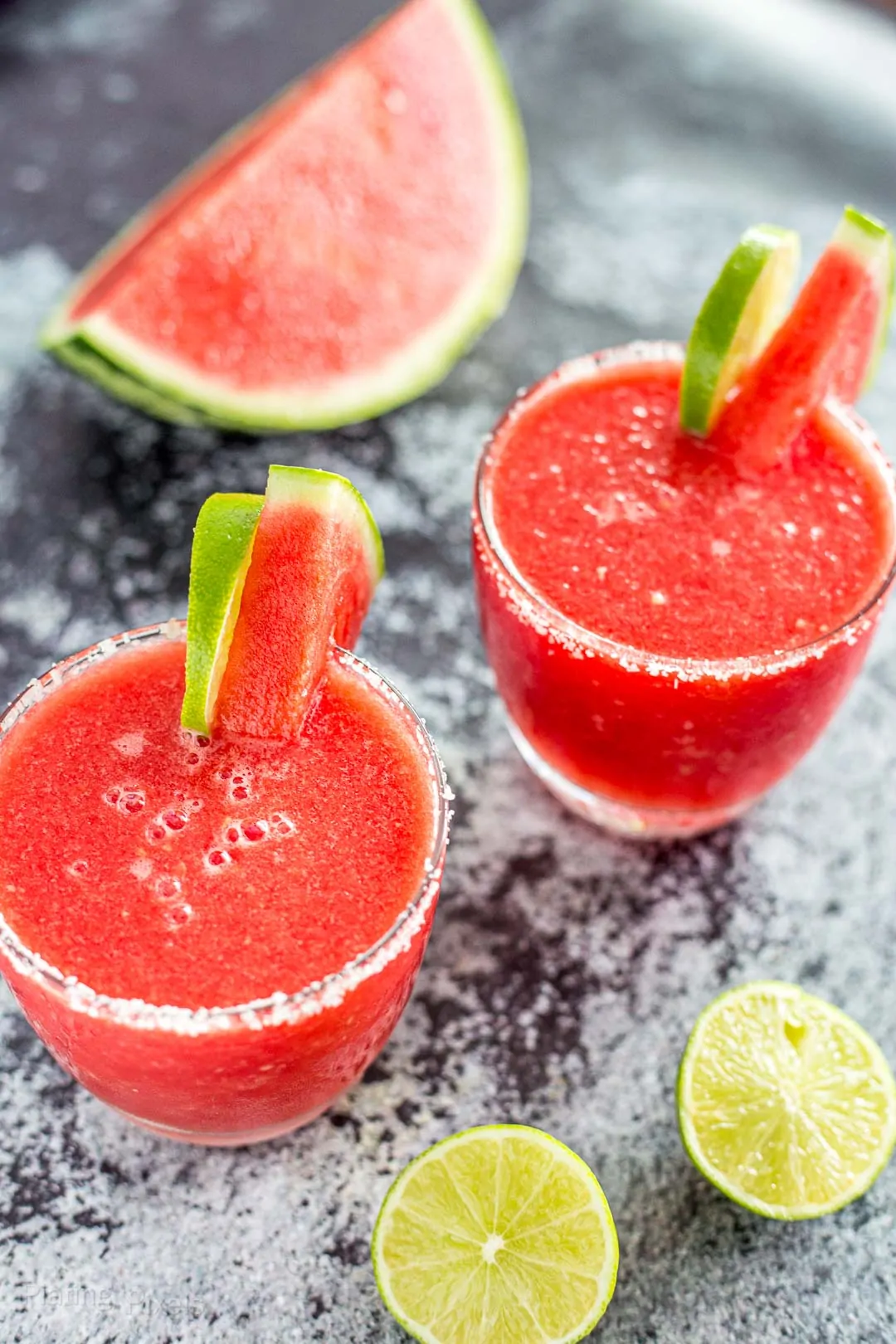 Two Frozen Watermelon Margaritas garnished with lime and watermelon wedges
