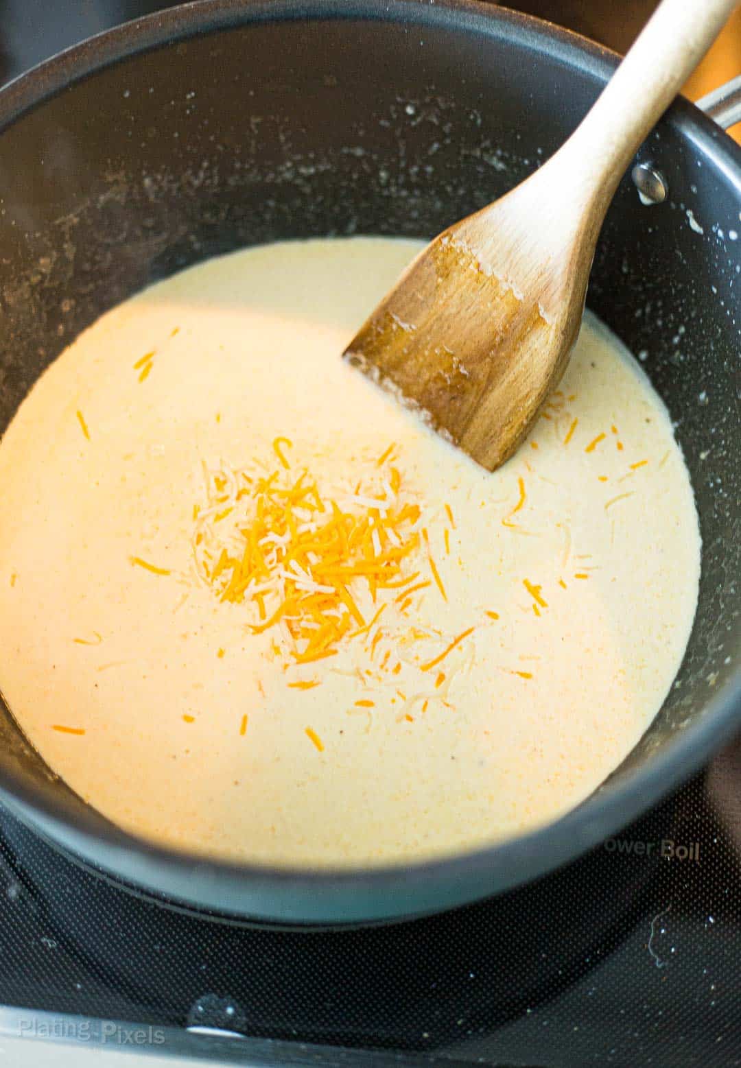 Process shot of adding shredded cheese to saucepan to make keto mac and cheese sauce