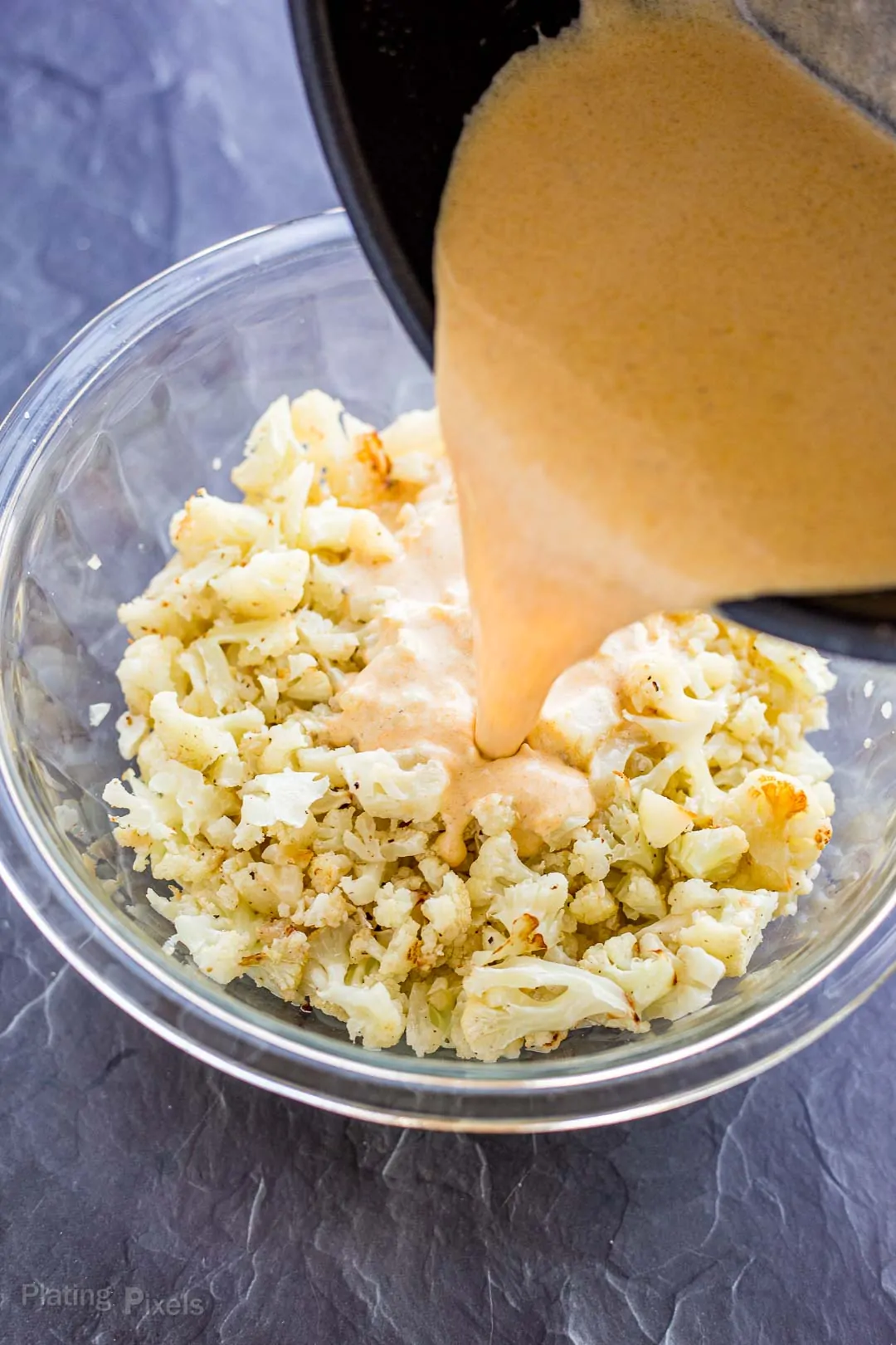 Process shot of pouring cheese sauce into a bowl of cauliflower pieces to make Cauliflower Mac and Cheese