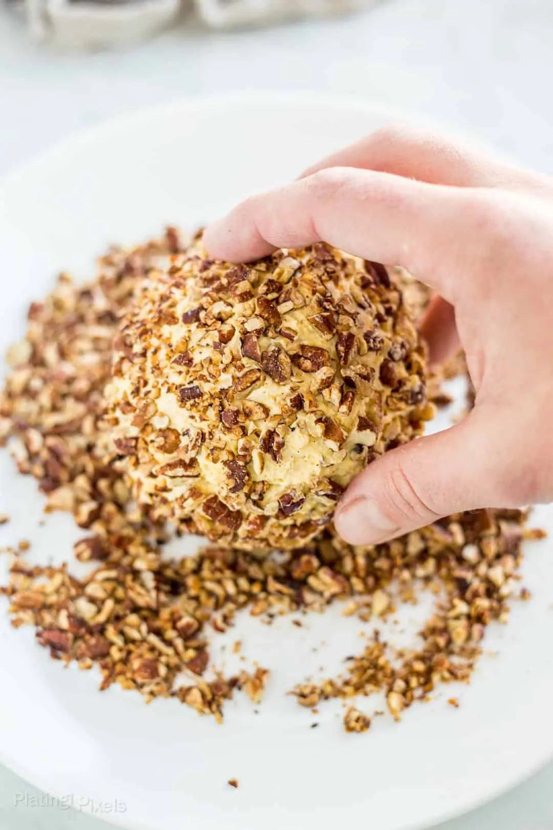 Process shot of rolling a Cheese Ball in chopped pecans