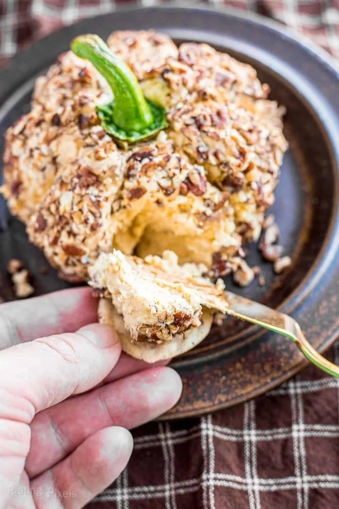 Using a cheese knife to spread some of cheese ball onto a cracker