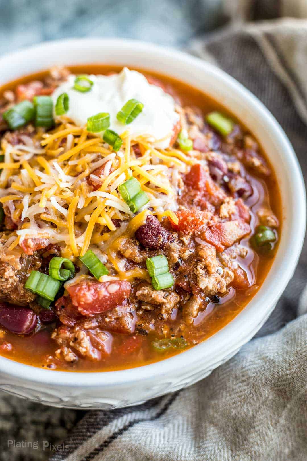 Healthy Turkey Chili in a bowl garnished with green onions, cheese and sour cream