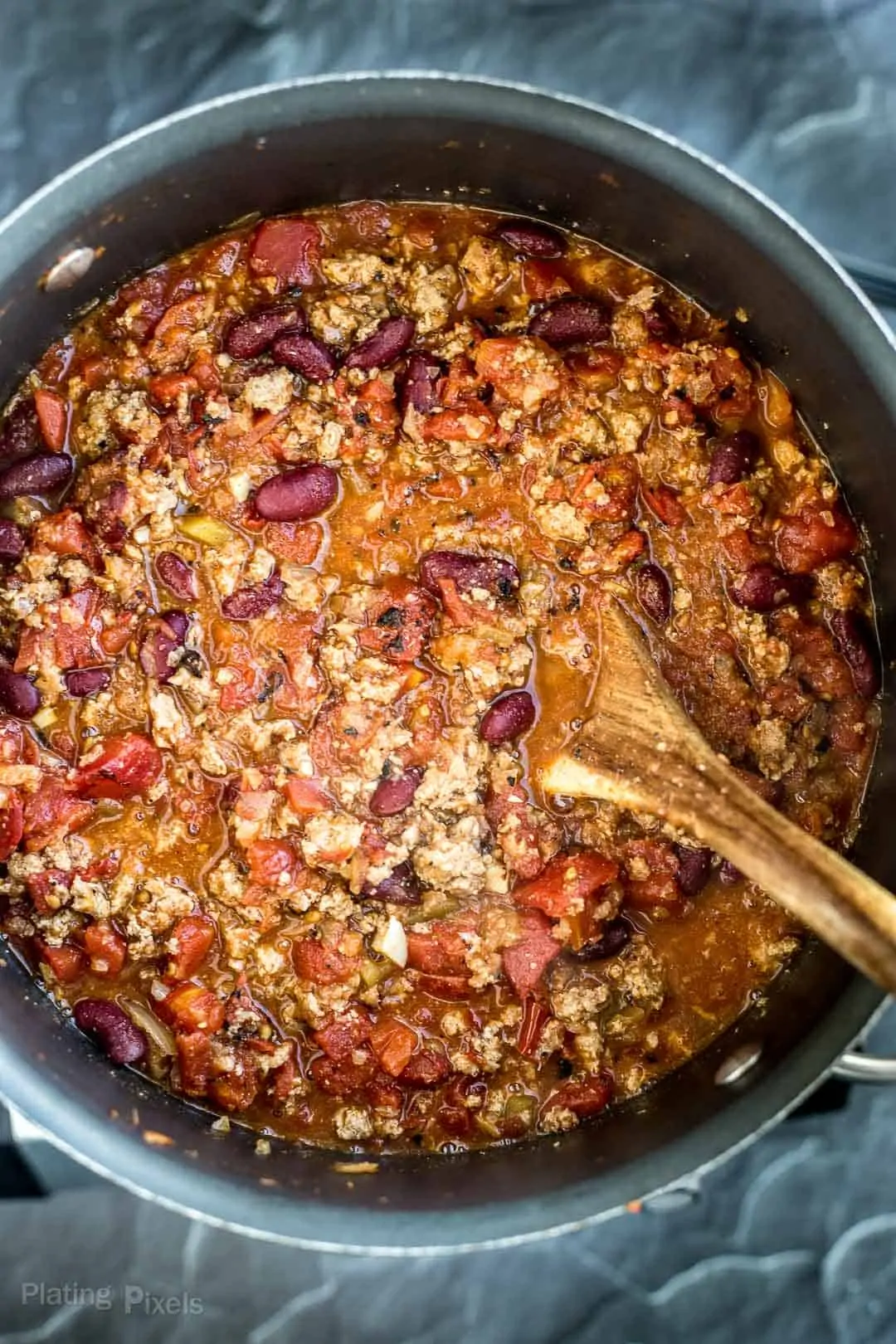 Process shot of adding canned diced tomatoes to turkey chili