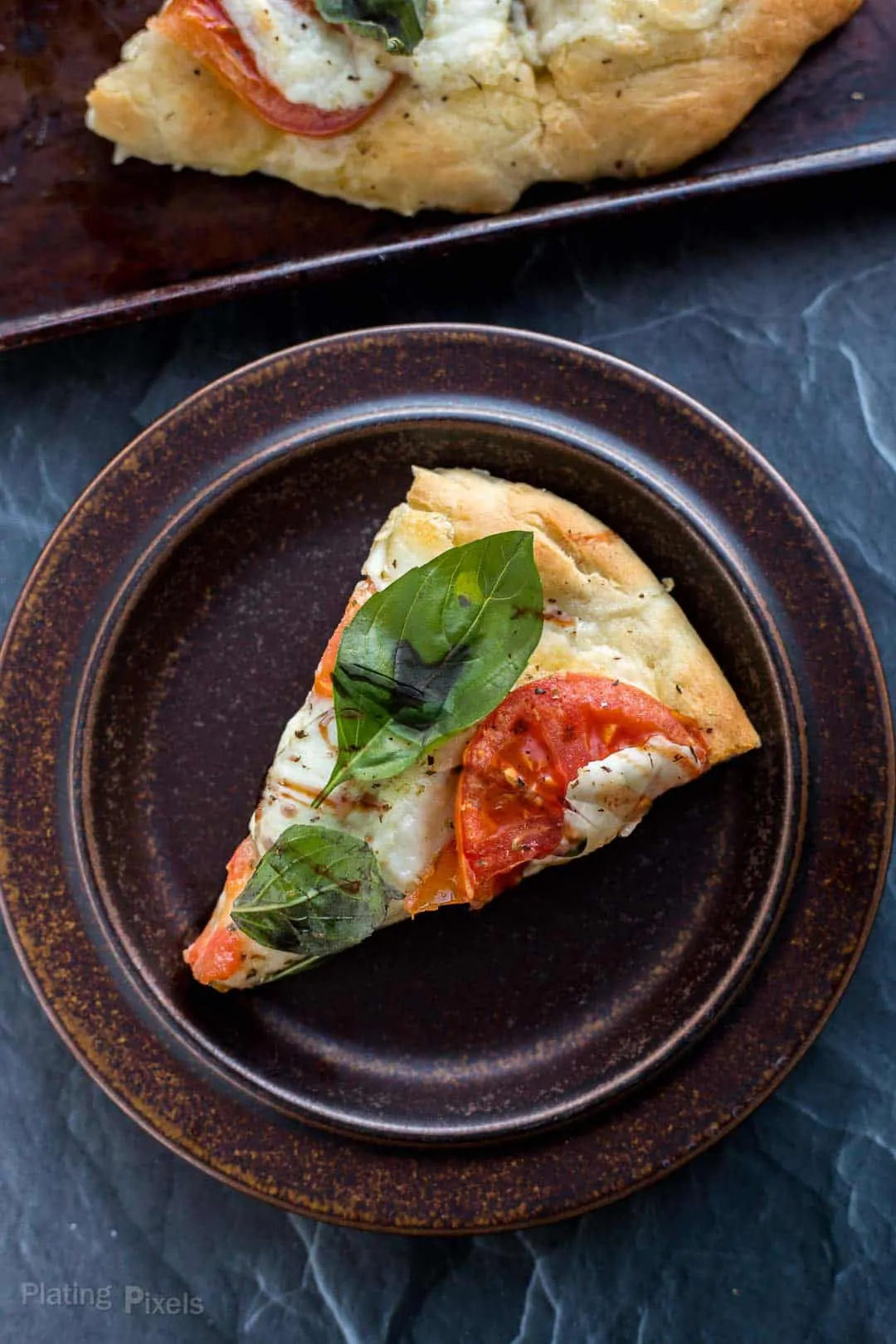 Slice of Caprese pizza on a brown plate