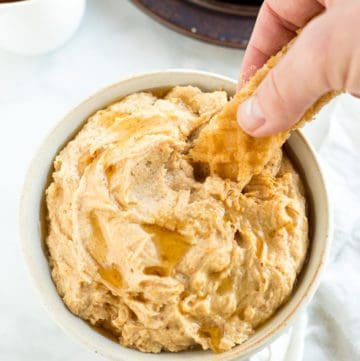 A hand dipping a waffle slice into peanut butter dip