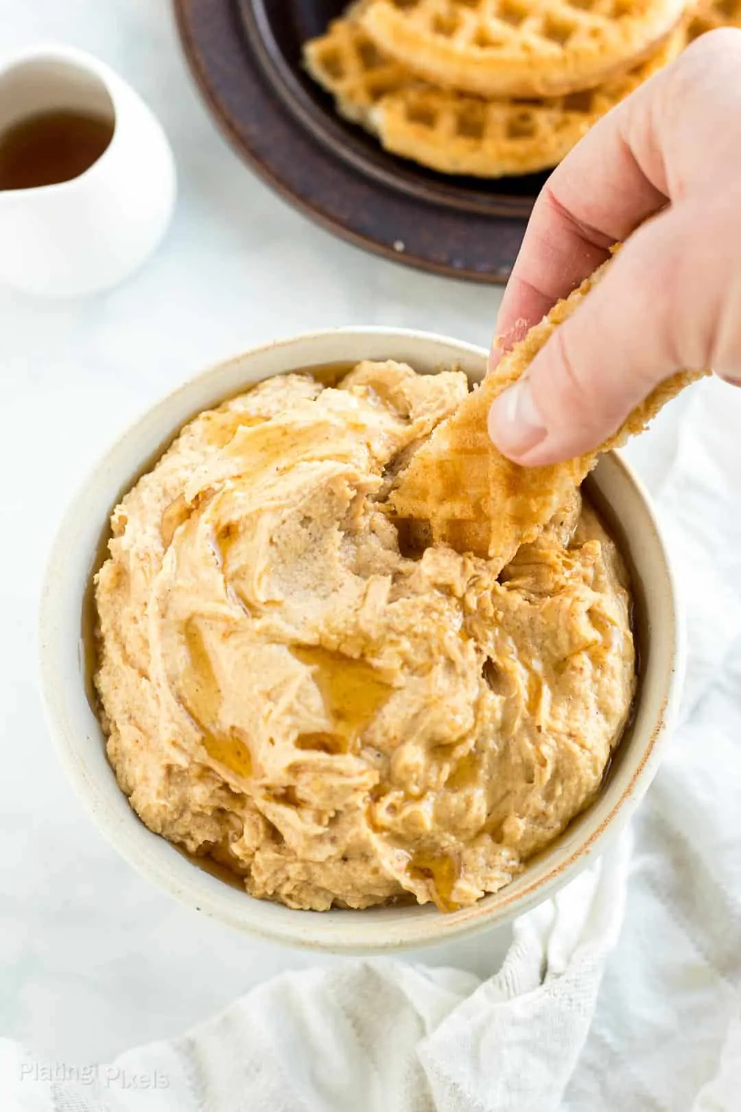 A hand dipping a waffle slice into peanut butter dip