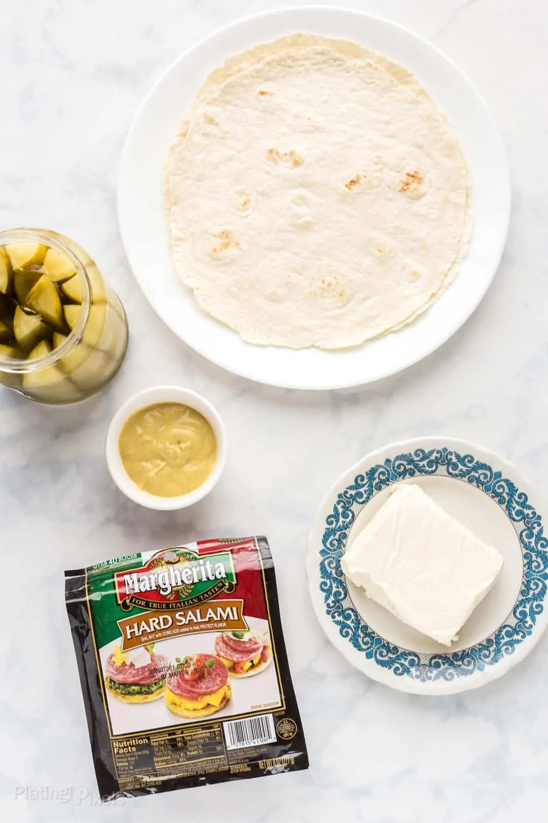 Prepared ingredients to make Salami Pinwheels on a white countertop