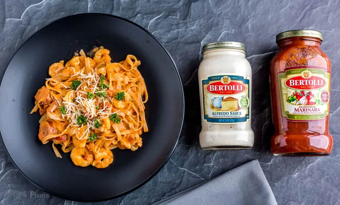 A plate of Shrimp and Sausage Spaghetti next to jars of Bertolli Sauces