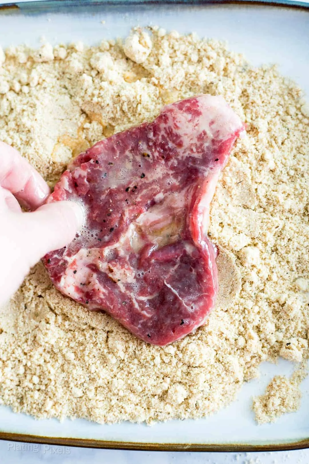 Process shot of coating one side of a cube steak into keto breading