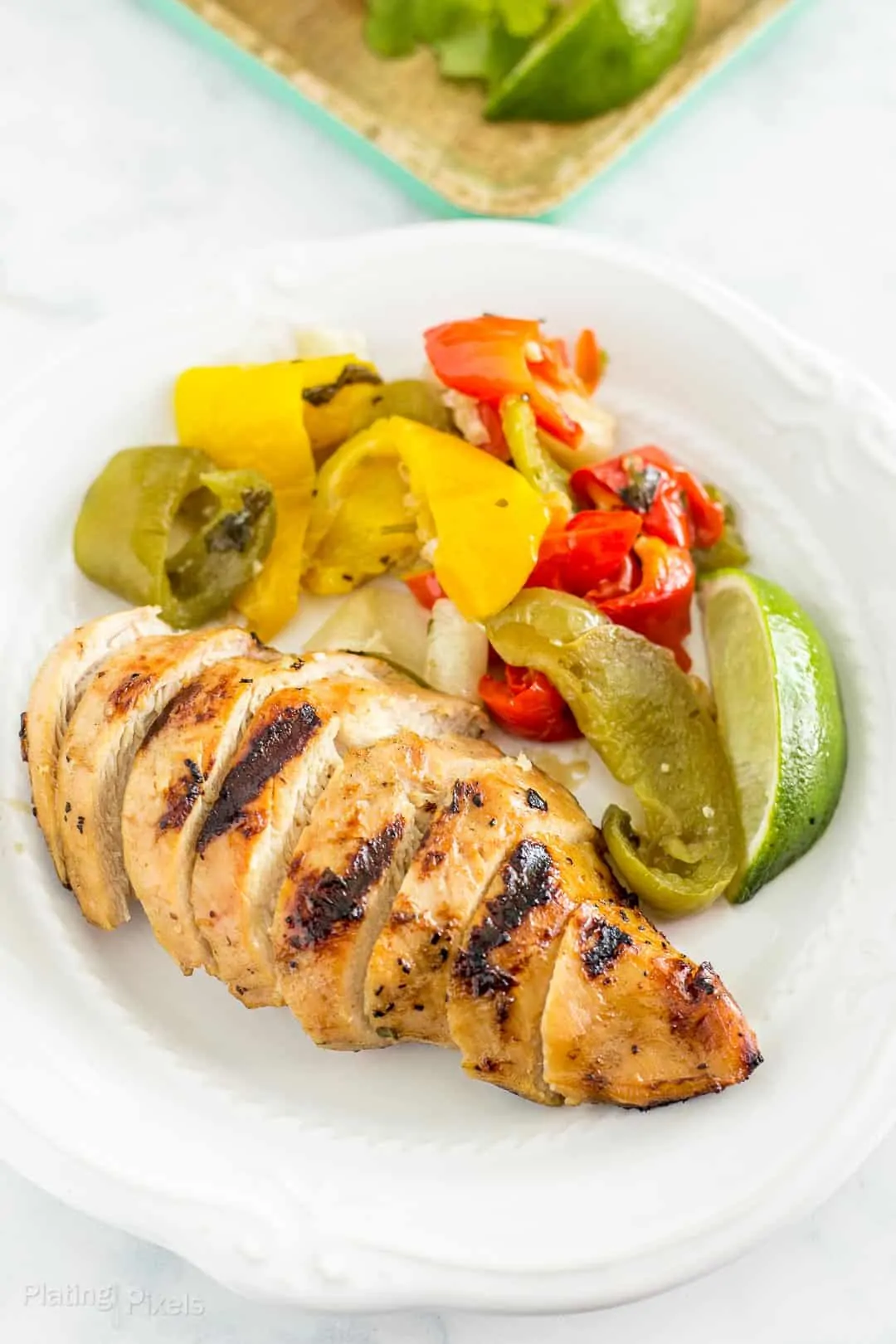 Sliced Grilled Chicken Fajitas on a plate next to the marinated vegetables