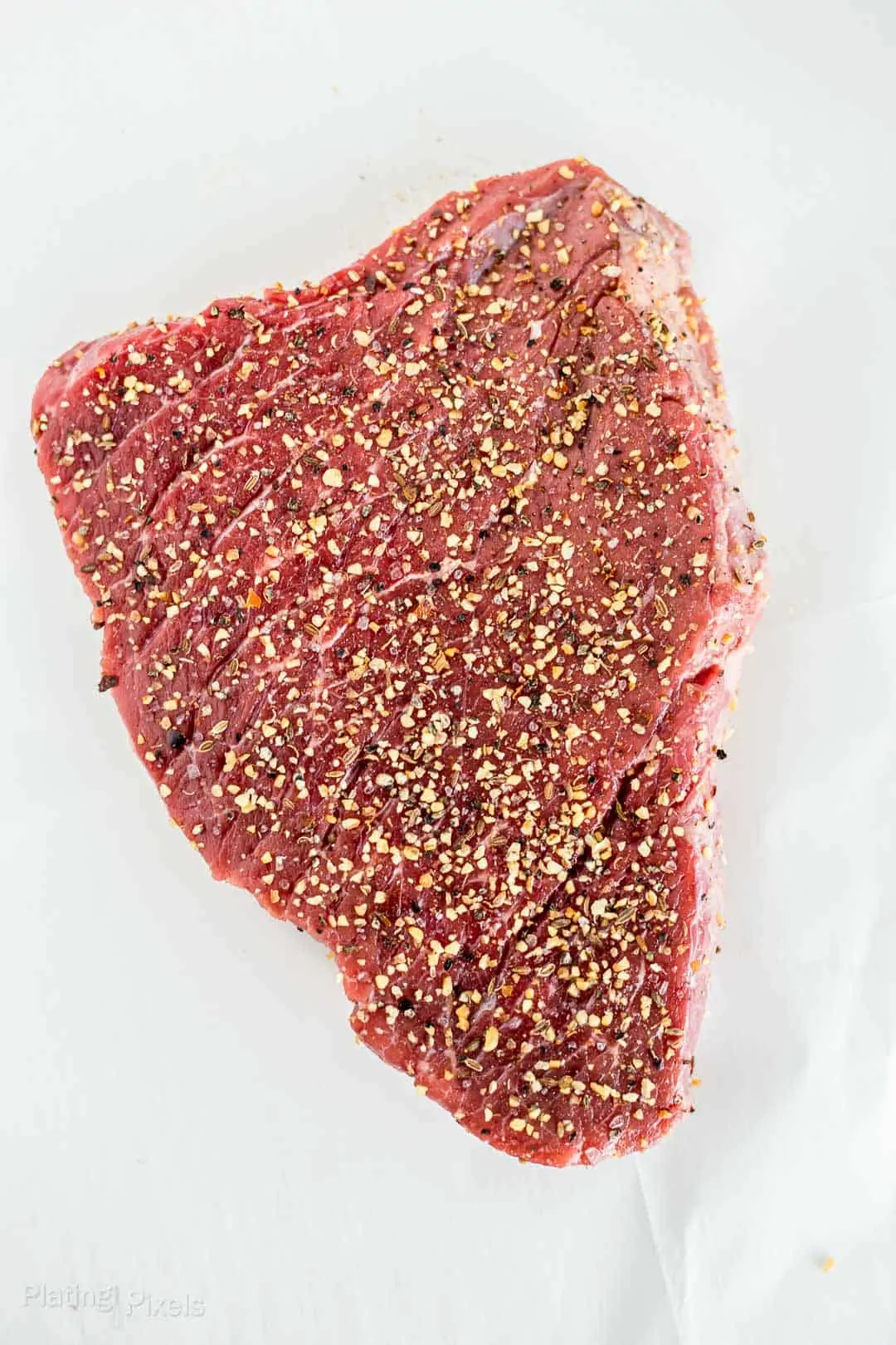 London Broil steak covered in steak seasoning and resting at room temp