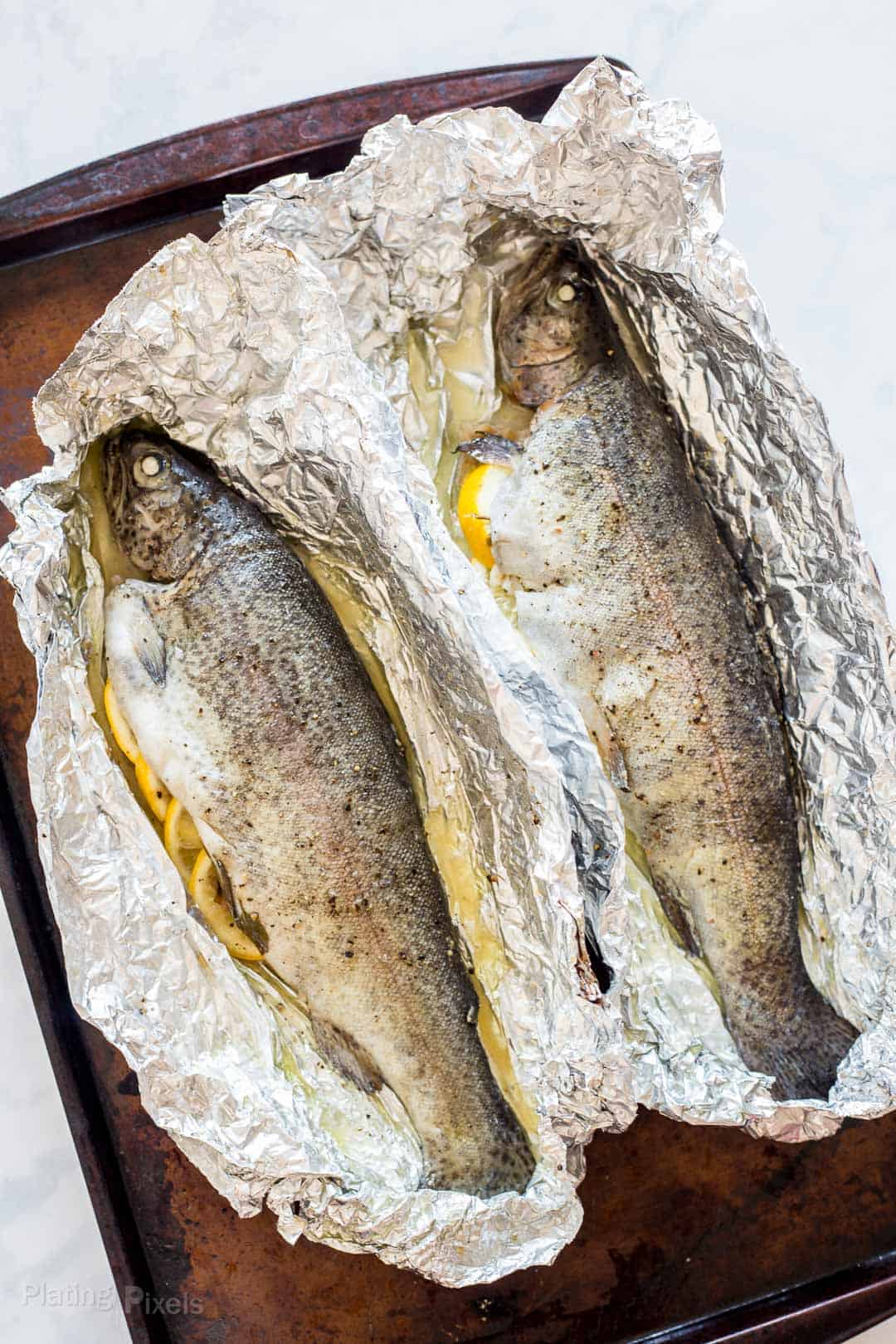 Two oven baked trouts on foil on a baking sheet