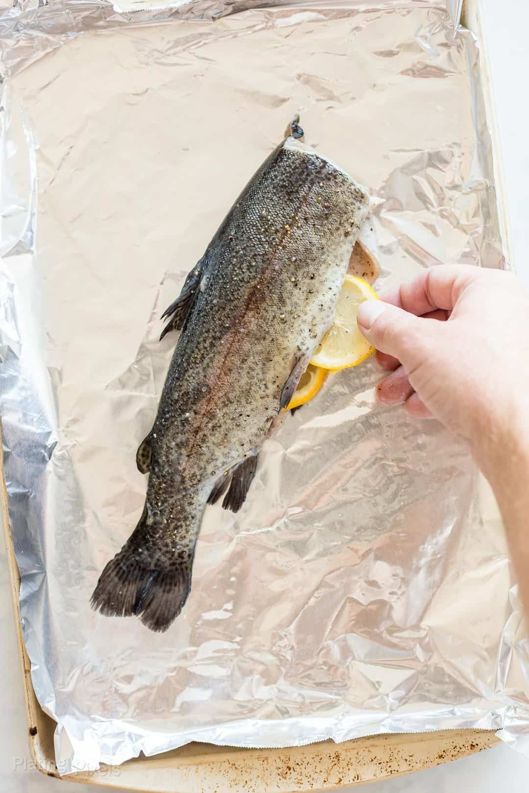 Process shot of inserting lemon slices into a whole trout