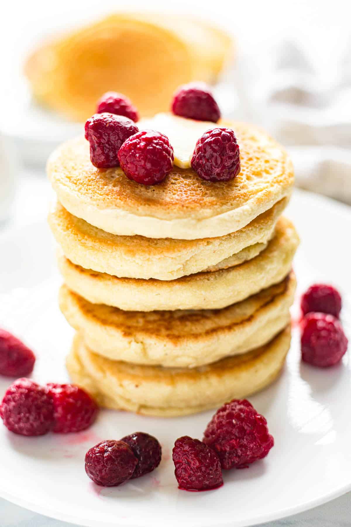 Stacked fluffy Keto Pancakes garnished with fresh raspberries